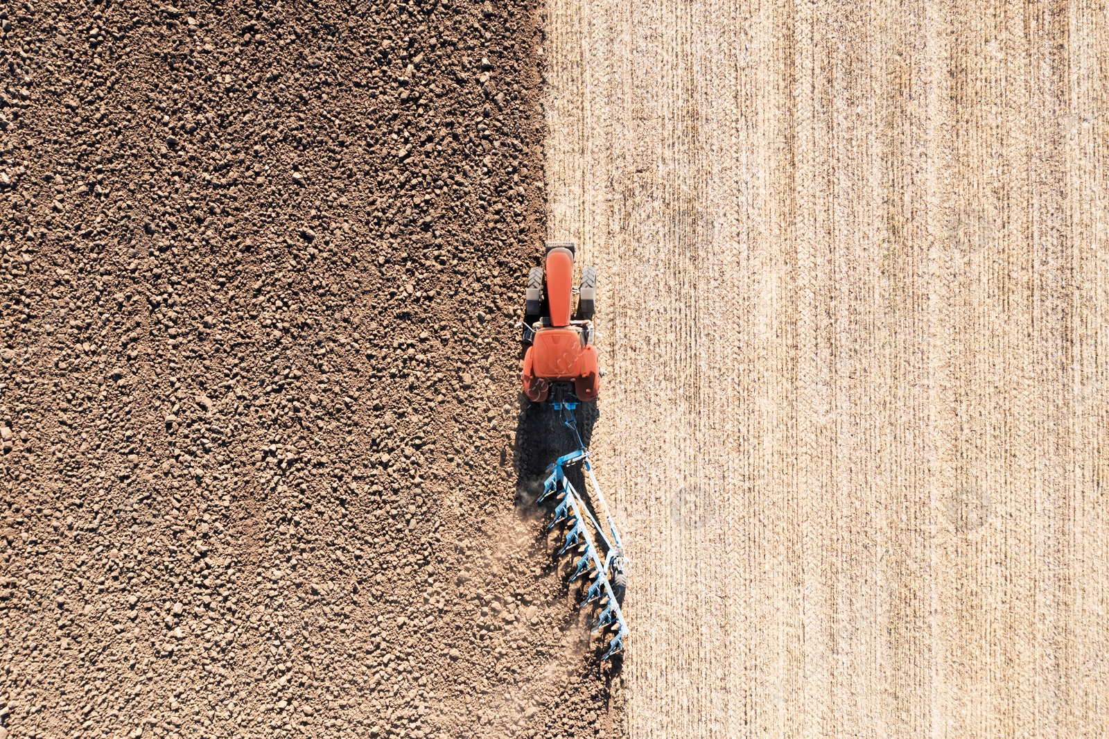 Image of Tractor pulling plow in agricultural field on sunny day, aerial view