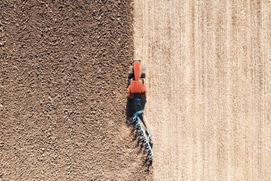 Image of Tractor pulling plow in agricultural field on sunny day, aerial view
