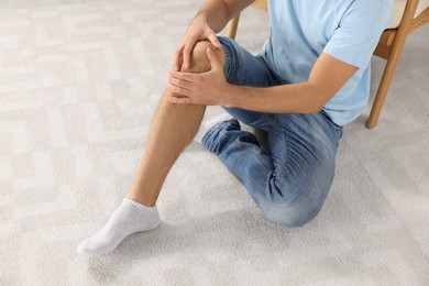 Photo of Man touching knee on white carpet near armchair, closeup