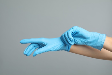 Doctor wearing medical gloves on grey background, closeup