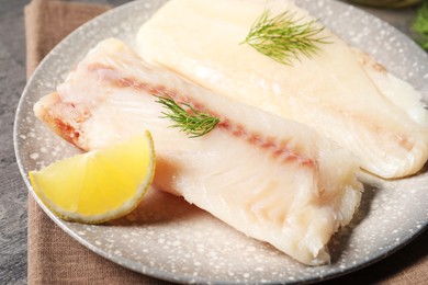 Photo of Pieces of raw cod fish, dill and lemon on table, closeup