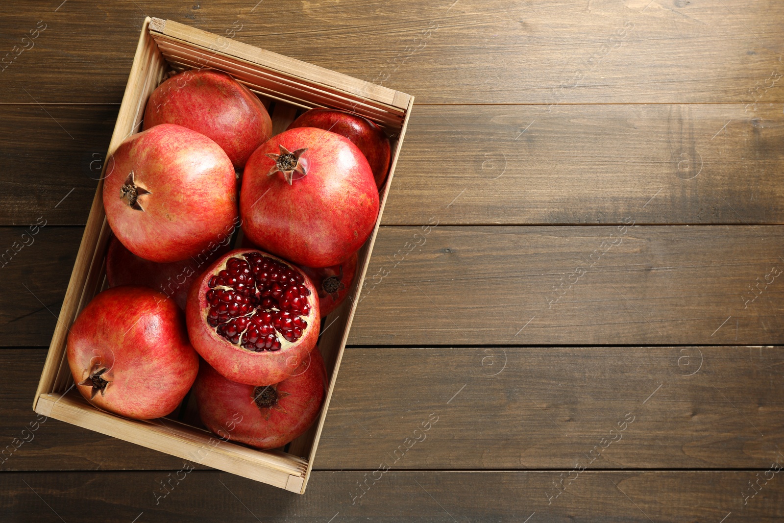 Photo of Ripe pomegranates in crate on wooden table, top view. Space for text