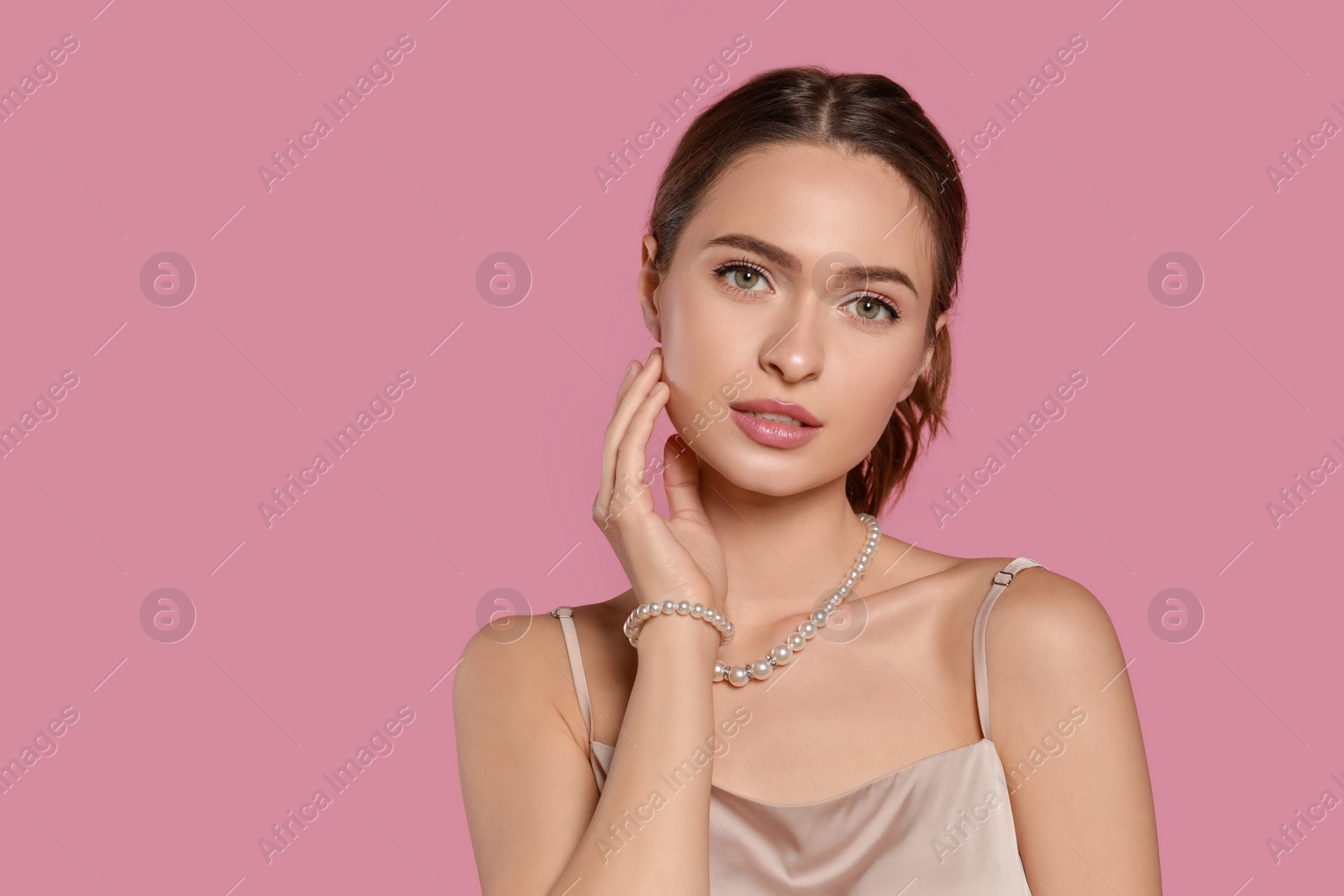 Photo of Young woman wearing elegant pearl jewelry on pink background, space for text