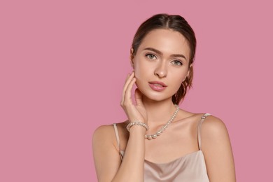Photo of Young woman wearing elegant pearl jewelry on pink background, space for text