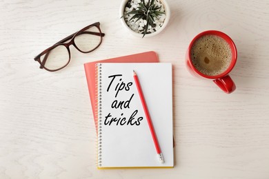 Notebook with text Tips and tricks on white wooden table, flat lay