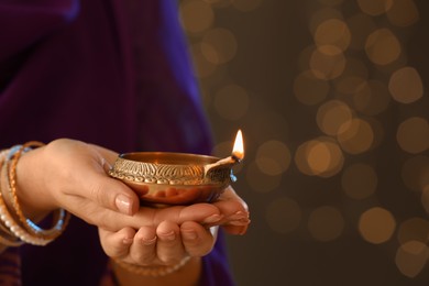Photo of Woman holding lit diya lamp in hands against blurred lights, closeup. Diwali celebration