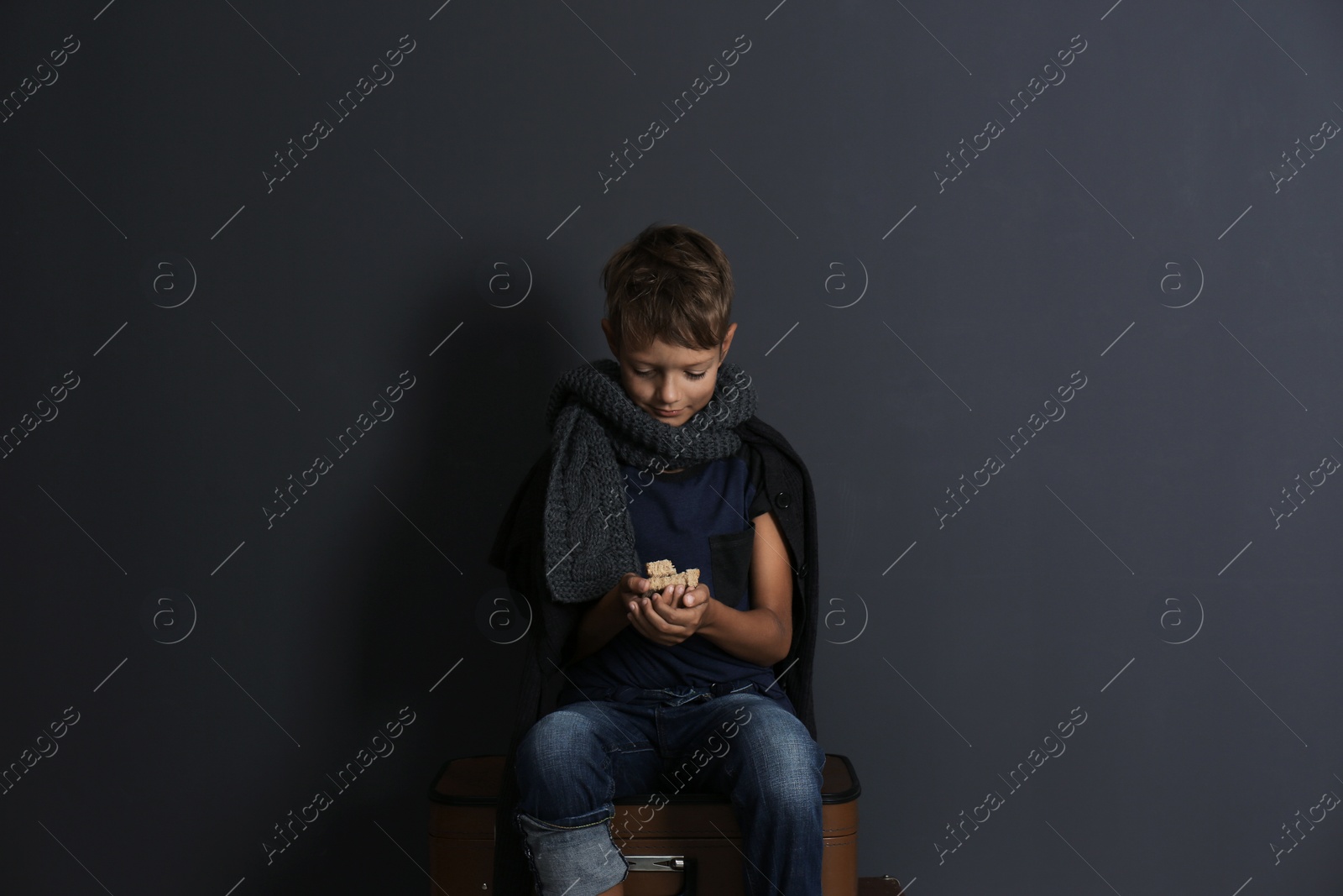 Photo of Poor boy with pieces of bread on dark background