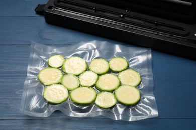 Photo of Sealer for vacuum packing and plastic bag with cut zucchinis on blue wooden table