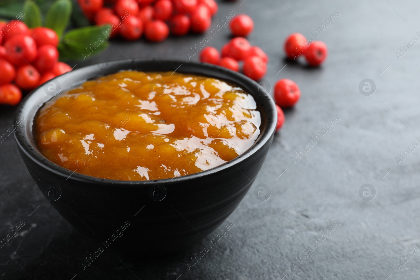 Photo of Delicious rowan jam in bowl on dark table, closeup. Space for text