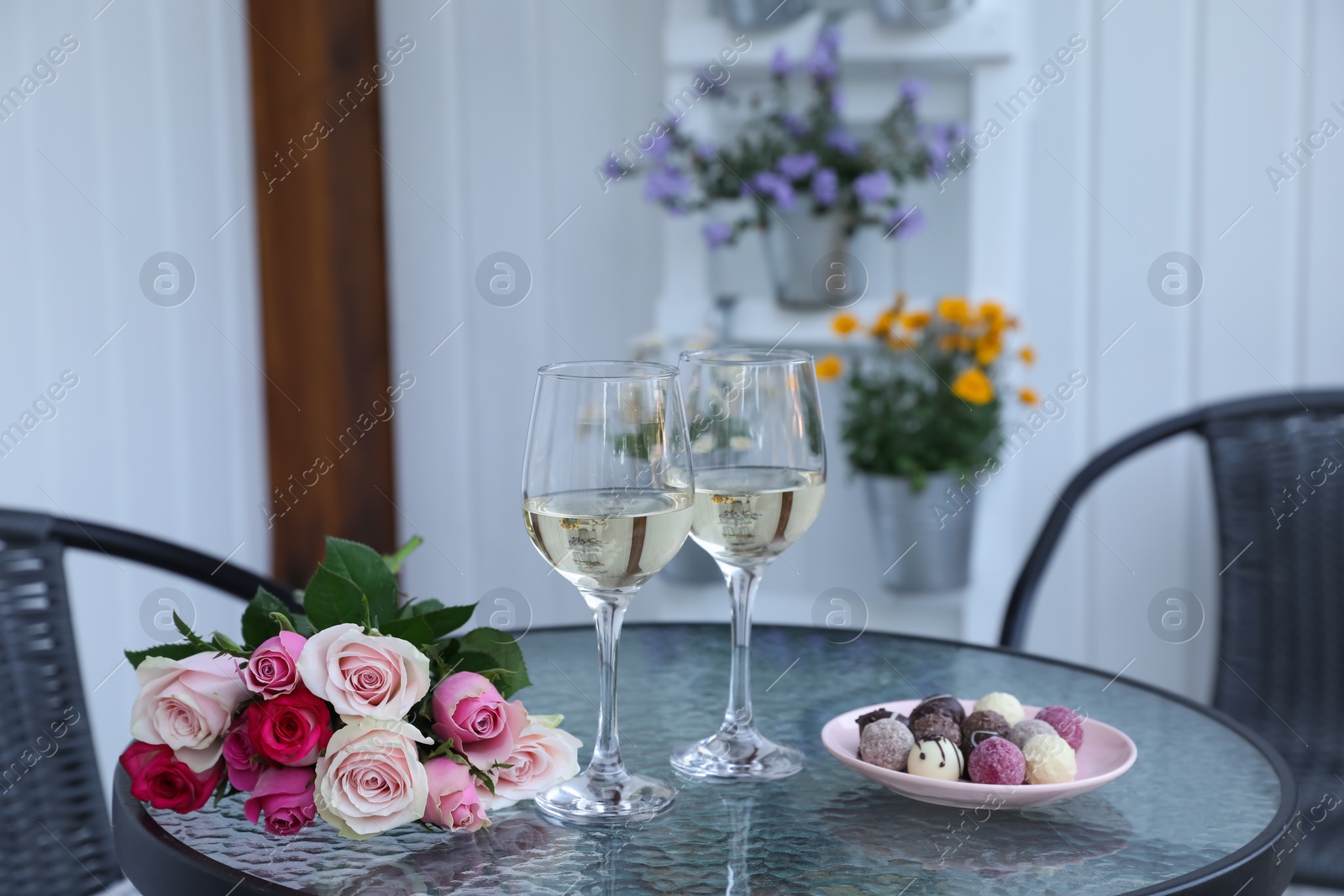 Photo of Bouquet of roses, glasses with wine and candies on glass table on outdoor terrace