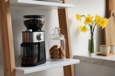 Photo of Modern coffee grinder and cookies on shelving unit in kitchen