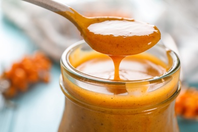 Spoon with delicious sea buckthorn jam over jar, closeup