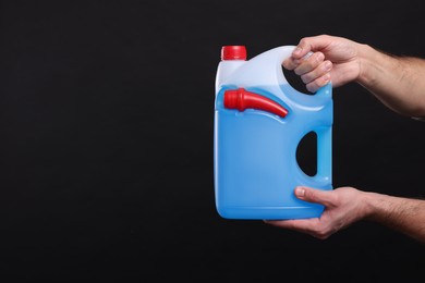 Photo of Man holding canister with blue liquid on black background, closeup. Space for text