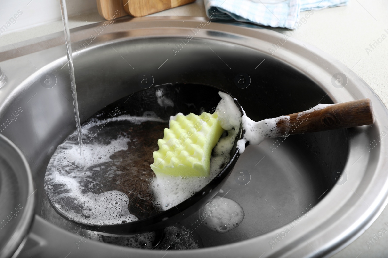 Photo of Dirty frying pan with sponge in kitchen sink, closeup