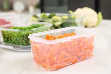 Photo of Plastic container with fresh carrots on white marble table, closeup. Food storage