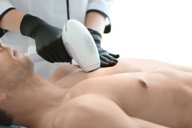 Photo of Man undergoing hair removal procedure with photo epilator in salon