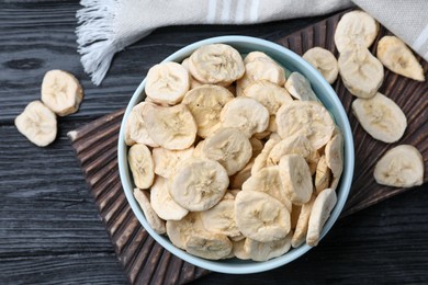 Photo of Bowl and dried banana slices on black wooden table, top view