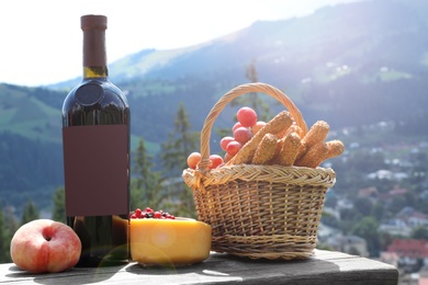 Bottle of red wine with ripe juicy grapes and other food for picnic on bench against mountain landscape