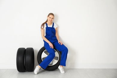 Female mechanic with car tires on light wall background