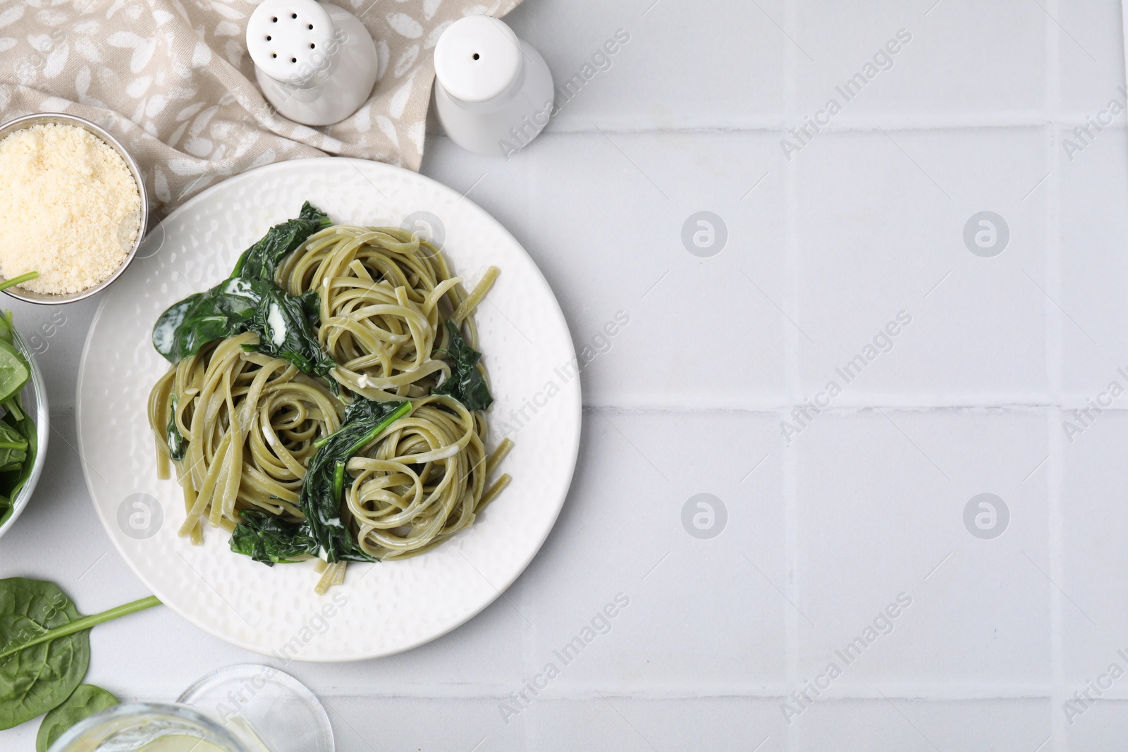 Photo of Tasty pasta with spinach and sauce served on white tiled table, flat lay. Space for text