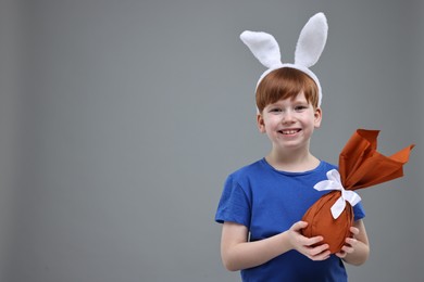 Photo of Easter celebration. Cute little boy with bunny ears and wrapped egg on grey background. Space for text