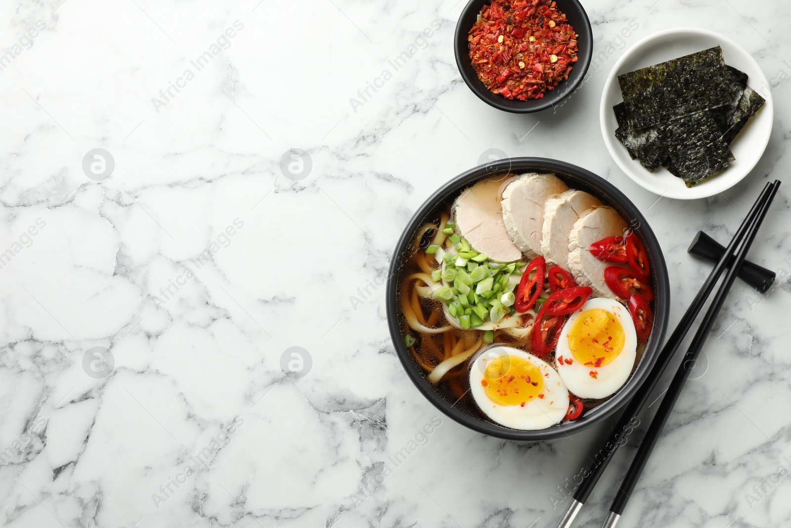 Photo of Delicious ramen in bowl served on white marble table, flat lay with space for text. Noodle soup