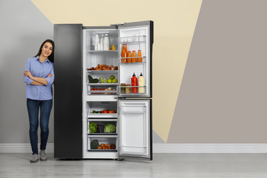 Happy young woman near open refrigerator indoors, space for text