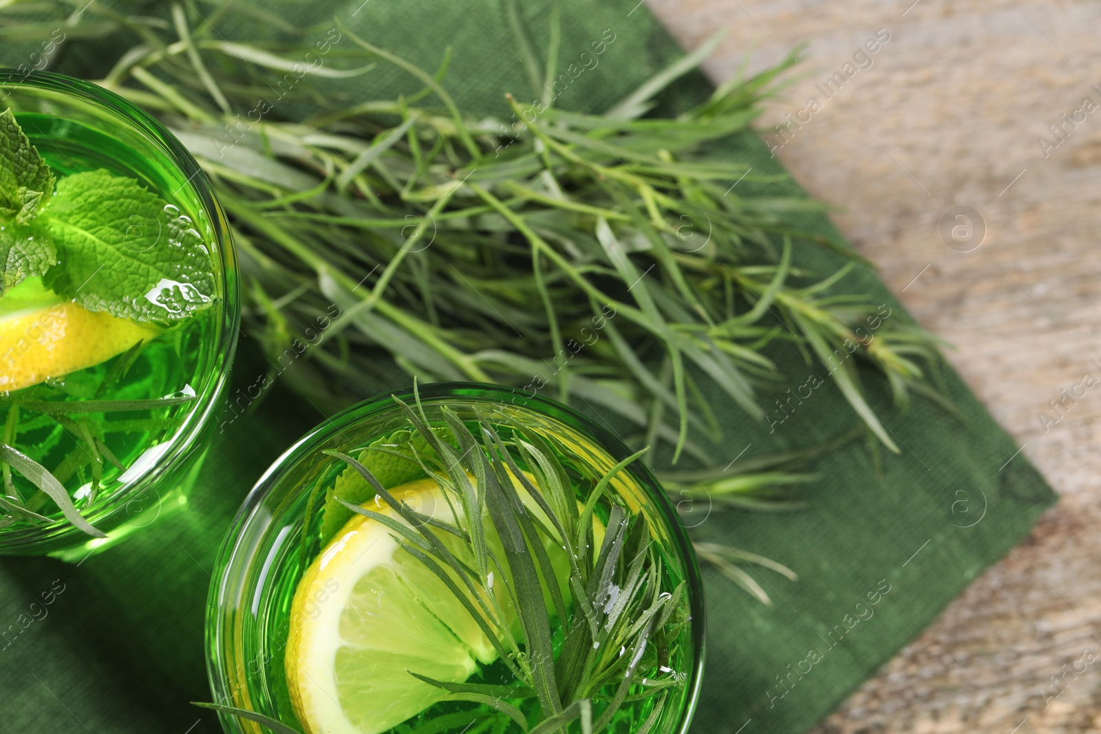 Photo of Glasses of refreshing tarragon drink with lemon slices on wooden table, flat lay. Space for text