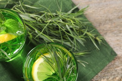 Glasses of refreshing tarragon drink with lemon slices on wooden table, flat lay. Space for text