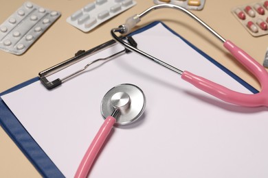 Photo of Stethoscope, clipboard and pills on beige background, closeup. Medical tool