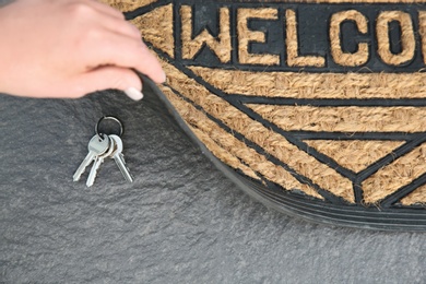 Photo of Young woman revealing hidden key under door mat, closeup