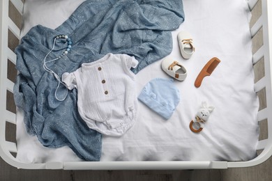 Flat lay composition with cute baby clothes and accessories on white bedsheet in crib