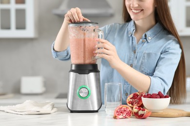 Beautiful young woman preparing tasty smoothie at white table in kitchen, closeup