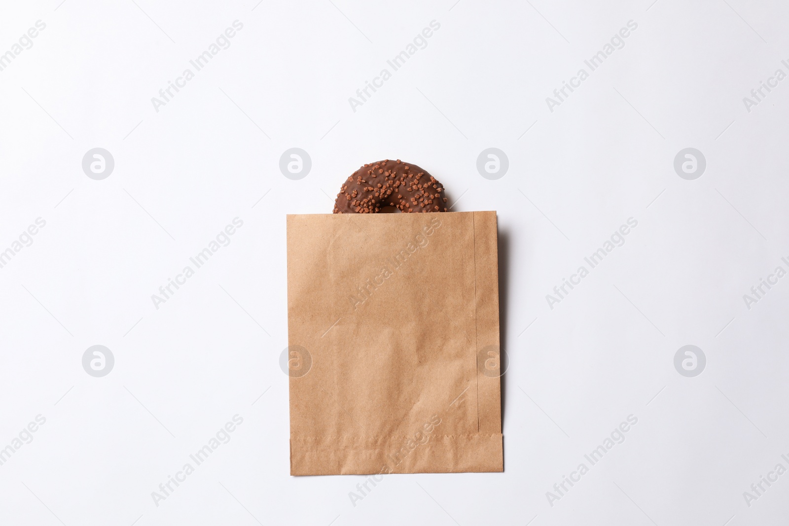 Photo of Paper bag with chocolate doughnut on white background, top view. Space for design