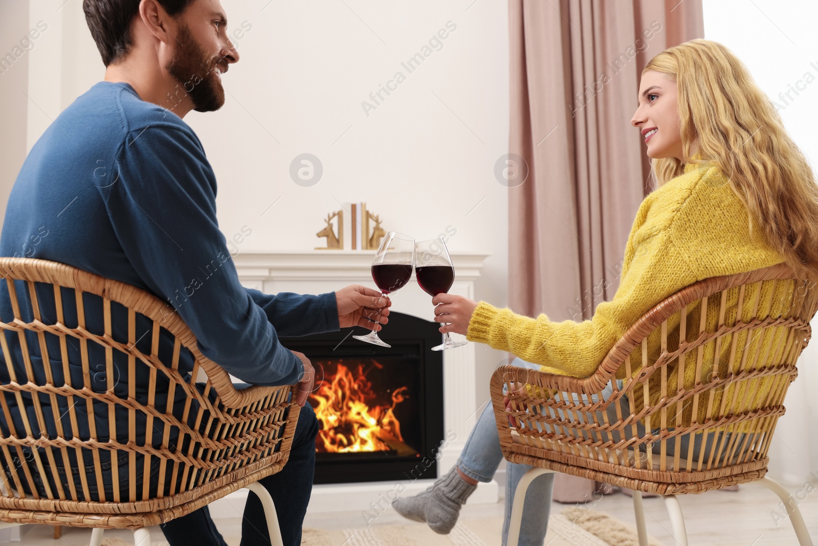 Photo of Lovely couple with glasses of wine spending time together near fireplace at home