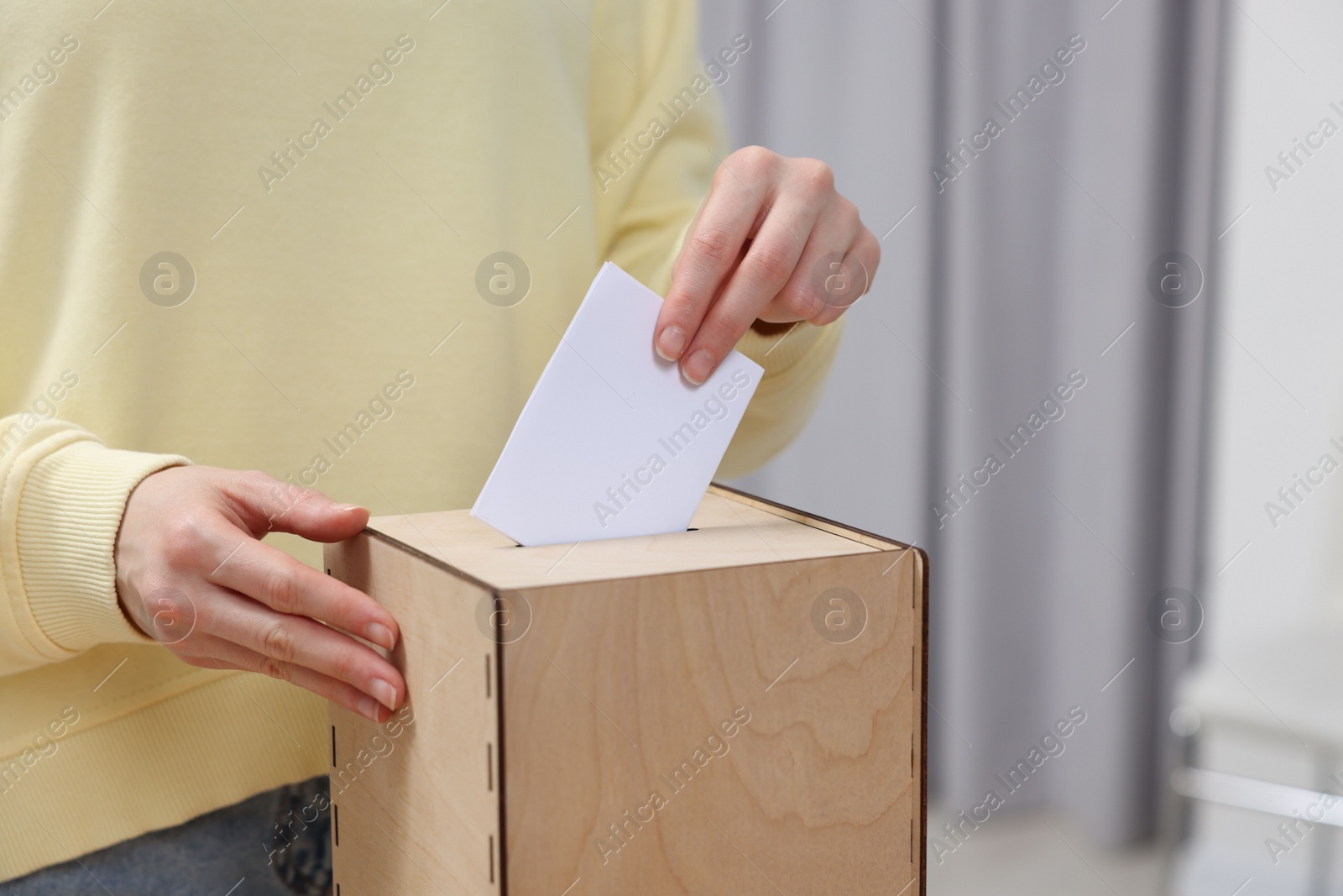 Photo of Woman putting her vote into ballot box on blurred background, closeup