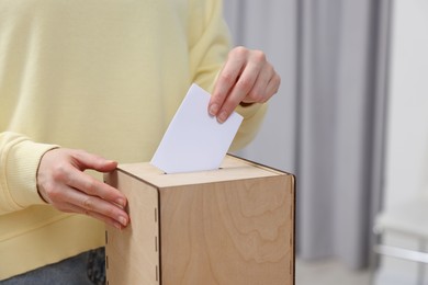 Photo of Woman putting her vote into ballot box on blurred background, closeup