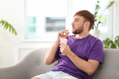 Photo of Young man with glass of delicious milk shake indoors