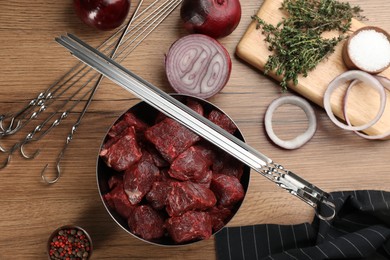 Flat lay composition with metal skewers and bowl of raw meat on wooden table