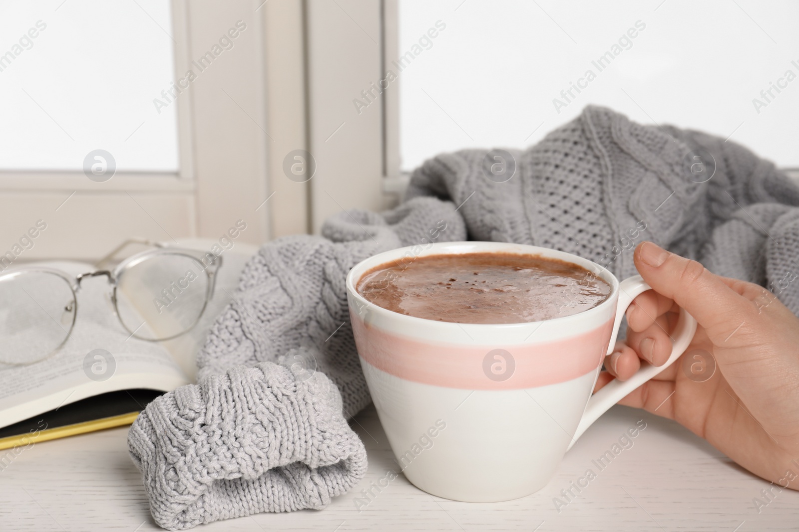 Photo of Woman holding cup of hot chocolate at window, closeup with space for text. Winter drink