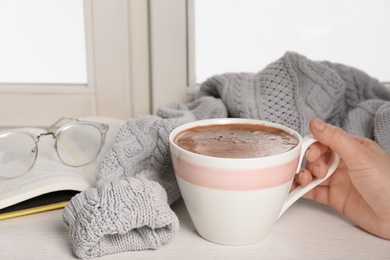 Photo of Woman holding cup of hot chocolate at window, closeup with space for text. Winter drink