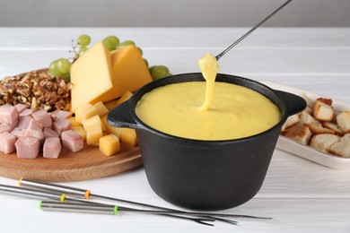 Photo of Dipping piece of ham into fondue pot with tasty melted cheese at white wooden table