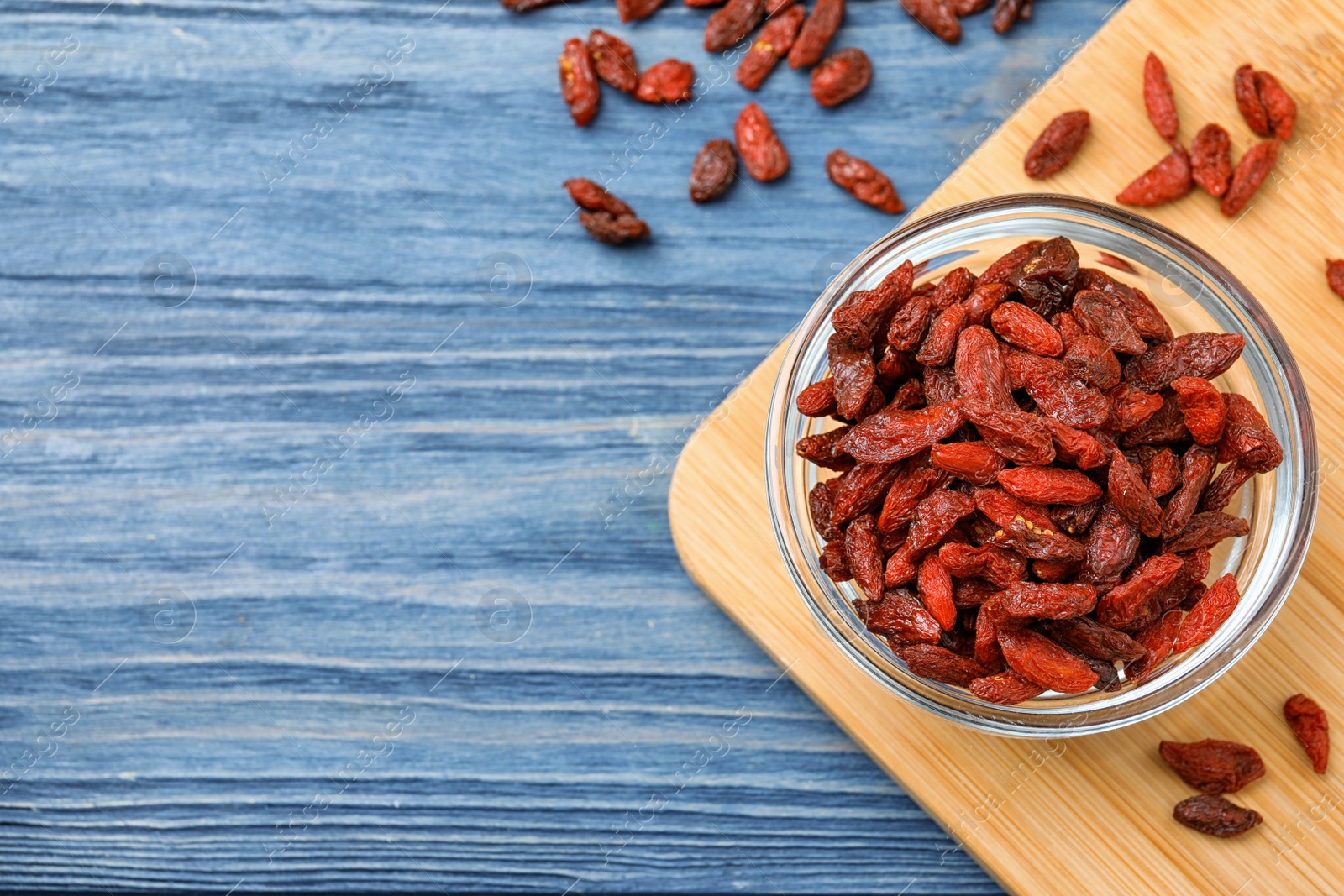 Photo of Dried goji berries on blue wooden table, flat lay. Space for text