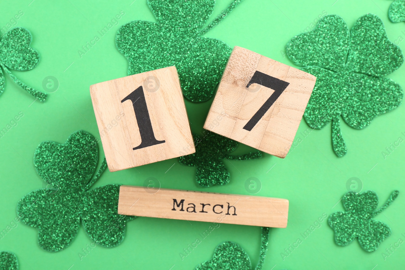 Photo of St. Patrick's day - 17th of March. Wooden block calendar and decorative clover leaves on green background, flat lay