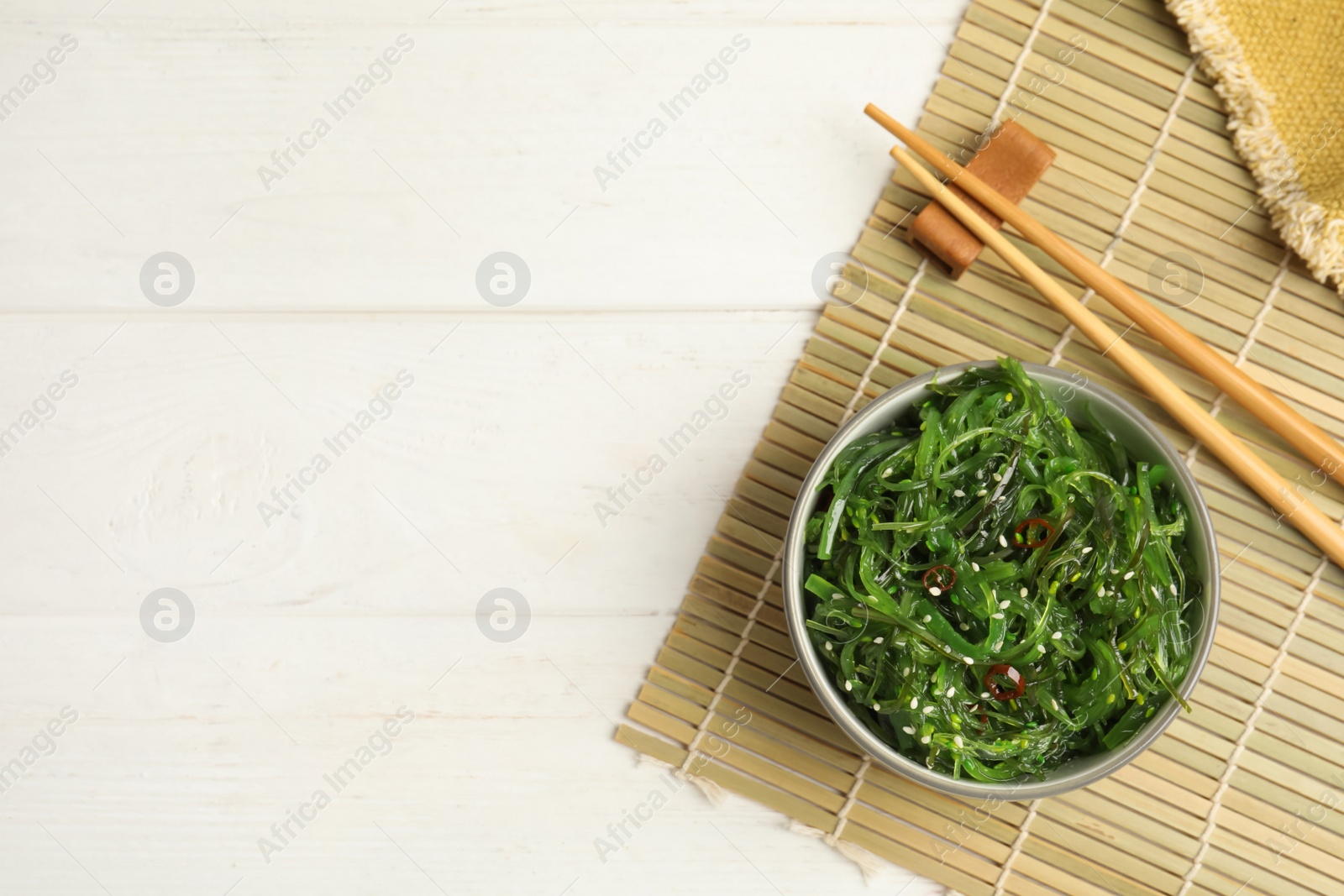 Photo of Japanese seaweed salad served on white wooden table, flat lay. Space for text