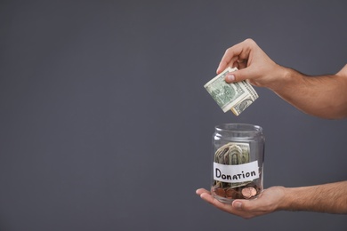 Photo of Man putting money into jar with label DONATION on grey background, closeup. Space for text