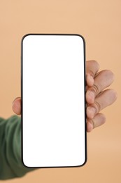 Man holding smartphone with blank screen on beige background, closeup