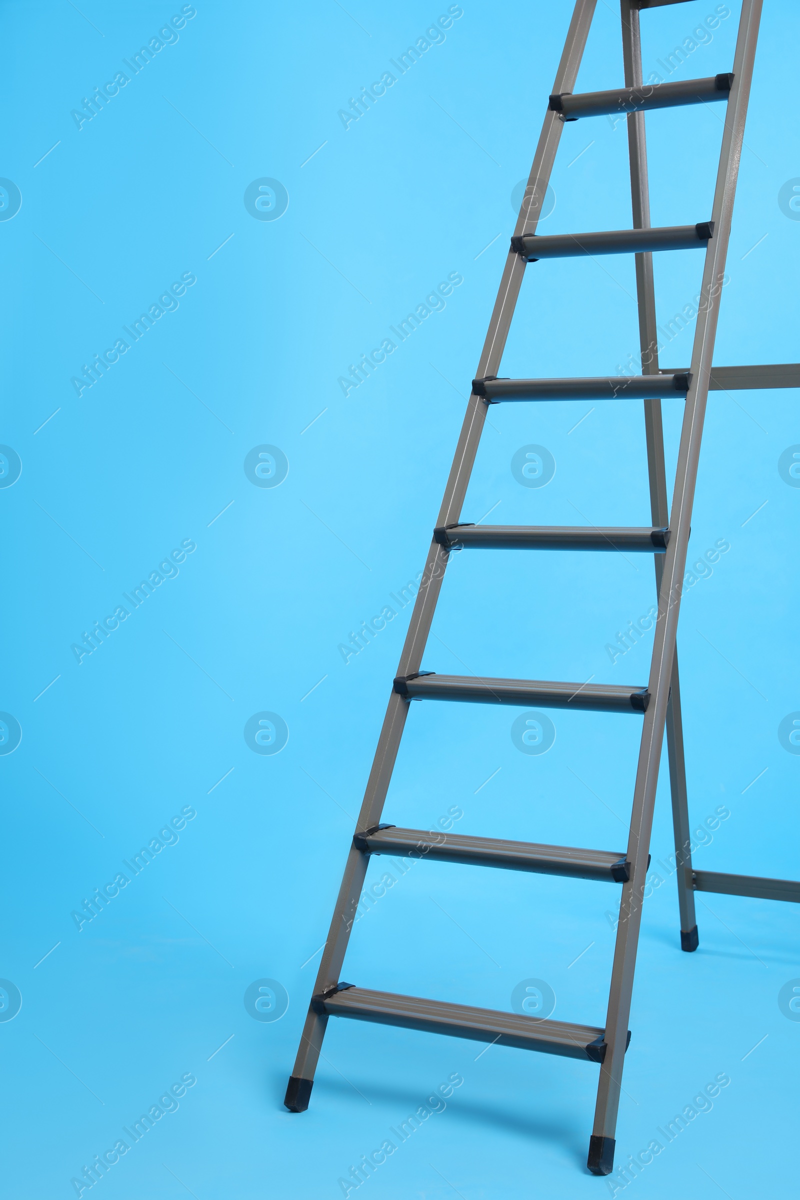 Photo of Metal stepladder on light blue background. Construction tool