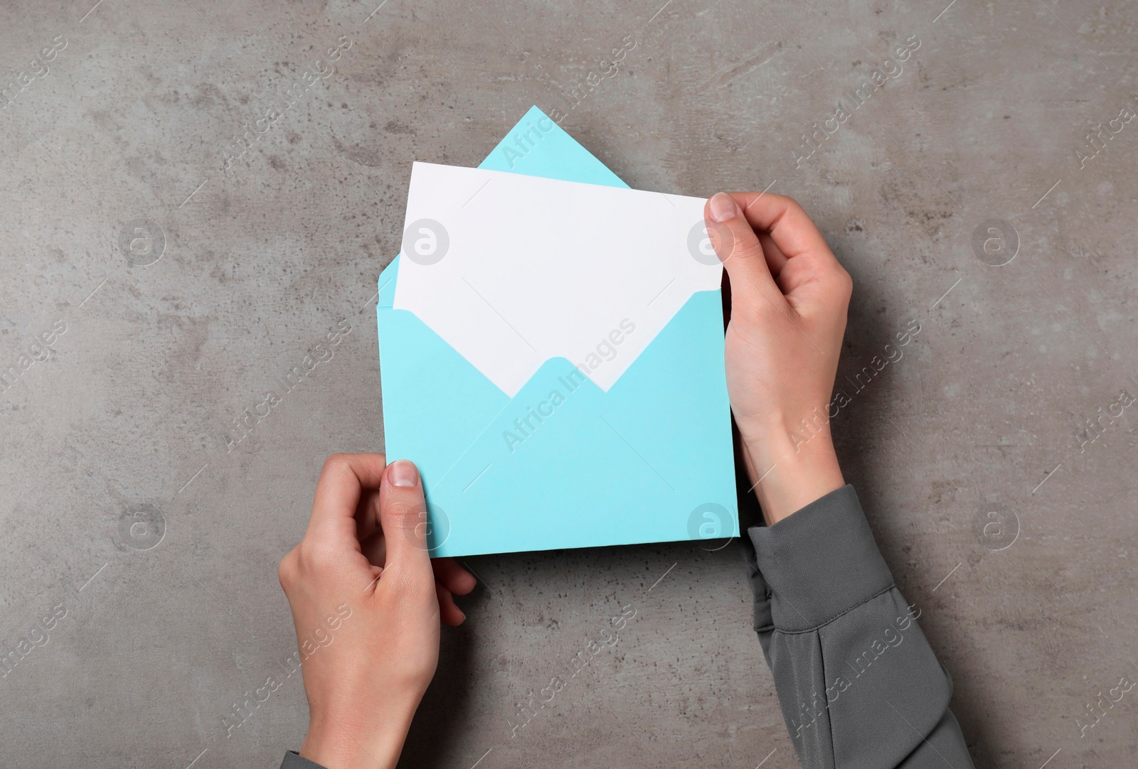 Photo of Woman holding letter envelope with card at grey textured table, top view