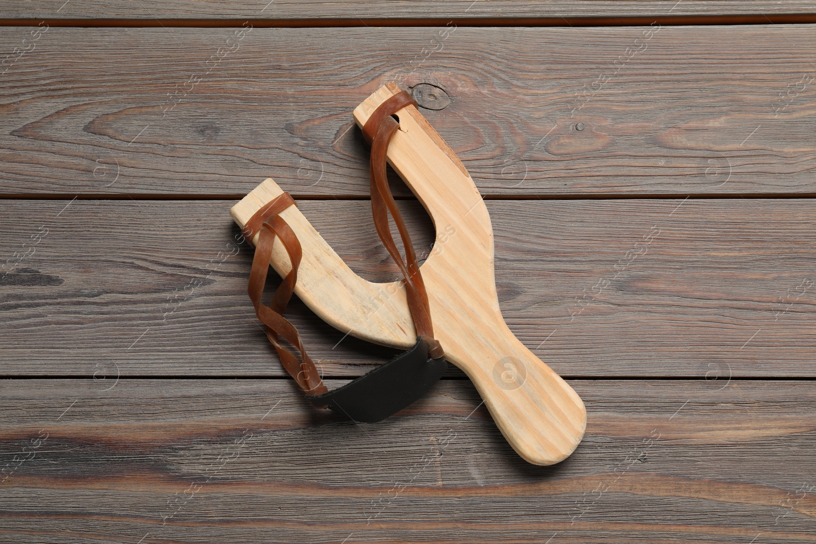 Photo of Slingshot with leather pouch on wooden background, top view